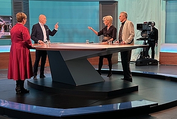 Volksanwältin Gaby Schwarz steht im ORF Studio neben einem Beschwerdeführer und spricht mit Moderator Peter Resetarits. 