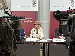 Volksanwältin Gaby Schwarz sitzt an einem Tisch bei einer Pressekonferenz, Kameras sind auf sie gerichtet.