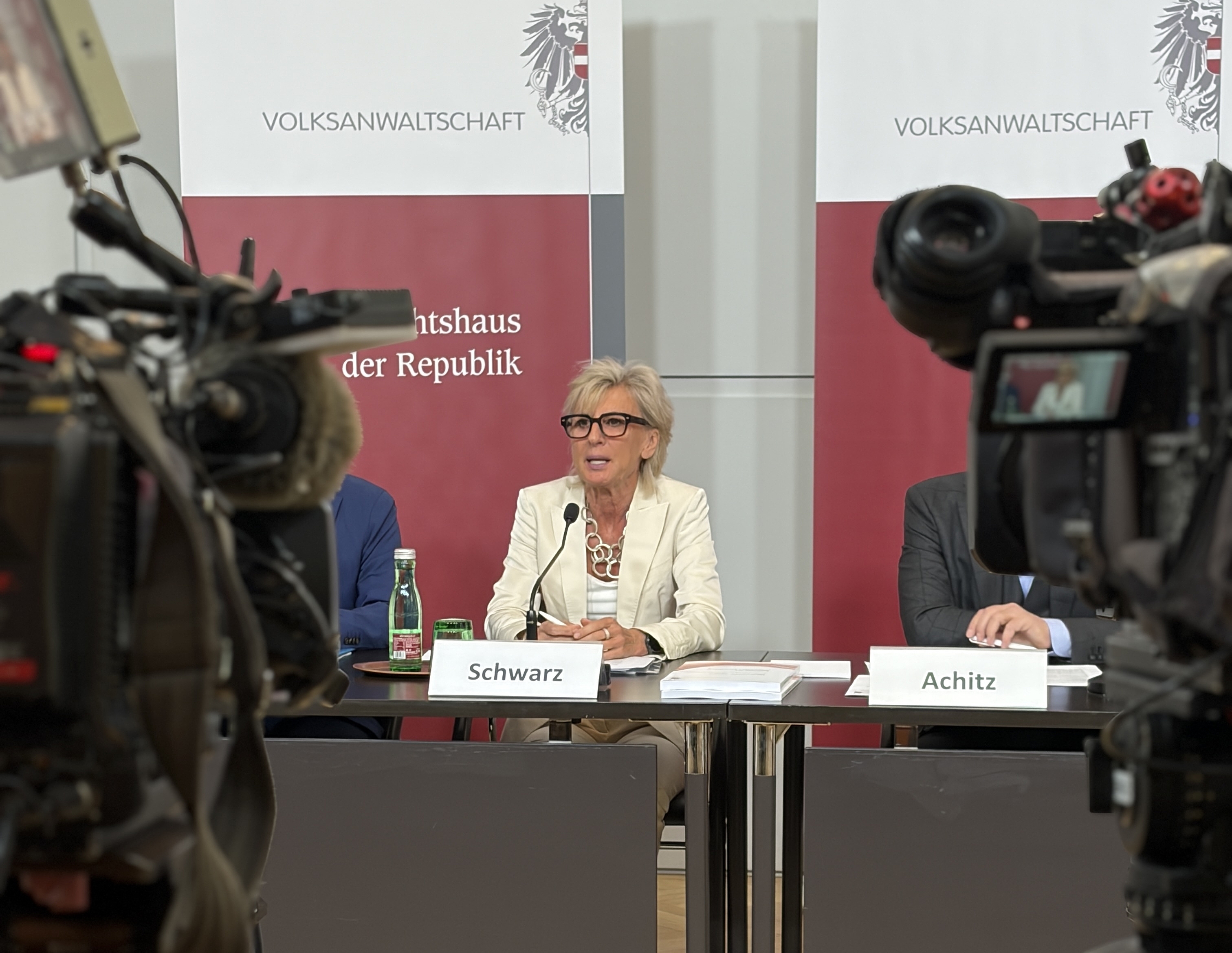 Volksanwältin Gaby Schwarz sitzt an einem Tisch bei einer Pressekonferenz, Kameras sind auf sie gerichtet.