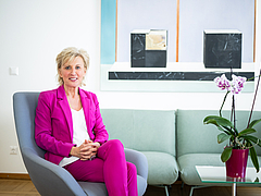 Ombudswoman Gaby Schwarz wears a pink trouser suit and sits in a turquoise armchair
