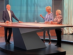 Ombudsperson Gaby Schwarz is standing in the public television channel ORF studio between the presenter and the complainant.