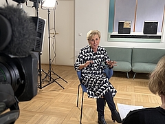 Ombudswoman Gaby Schwarz sits on a chair in her office and gives a TV interview.