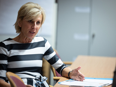 People's Advocate Gaby Schwarz in a black and white striped dress, sitting at a table and talking to another person.