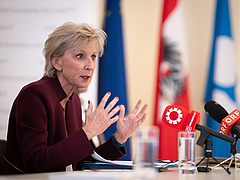 Volksanwältin Gaby Schwarz sitzt an einem Tisch und spricht in Mikros.