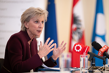 Volksanwältin Gaby Schwarz sitzt an einem Tisch und spricht in Mikros.