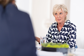 Volksanwältin Gaby Schwarz sitzt an einem Tisch, im Gespräch mit einer anderen Person
