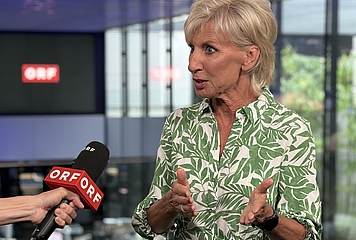 Volksanwältin Gaby Schwarz in einem grün-weißen Kleid, wird von einer ORF Redakteurin interviewt und spricht in ein Mikrofon.