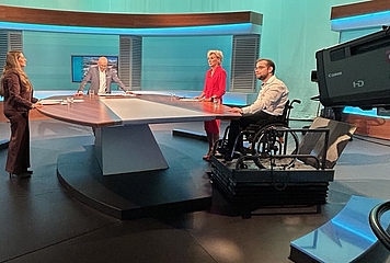 4 people are standing in the ORF studio, including Ombudswoman Gaby Schwarz and next to her the complainant in a wheelchair.