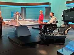 4 people are standing in the ORF studio, including Ombudswoman Gaby Schwarz and next to her the complainant in a wheelchair.