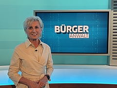 Volksanwältin Gaby Schwarz steht in einem beigen Kleid im ORF Studio vor dem Bürgeranwalt Logo.