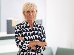 Ombudswoman Gaby Schwarz stands in her office with her arms folded, wearing a black and white dress.