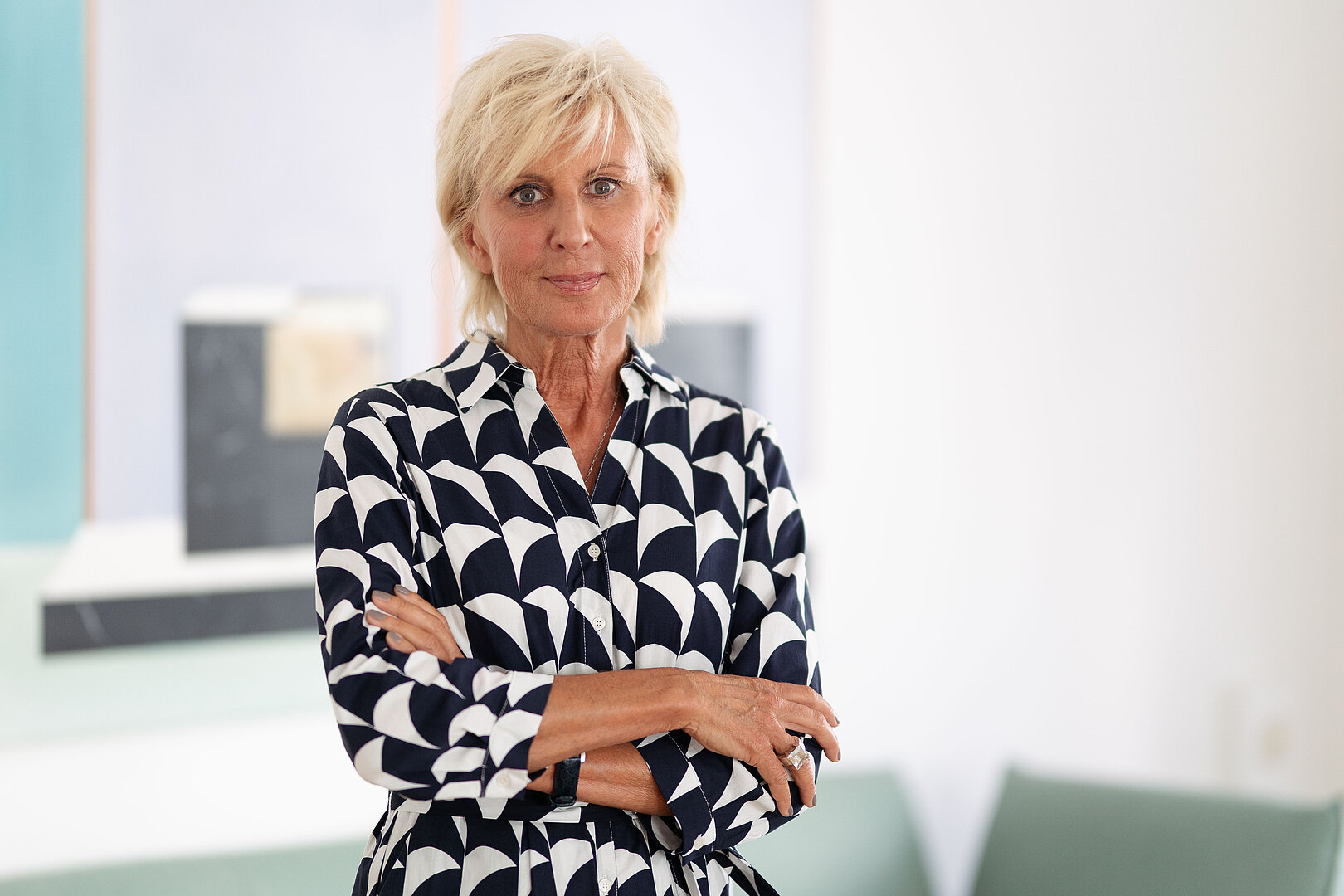 Volksanwältin Gaby Schwarz steht mit verschränkten Armen in einem schwarz/weißen Kleid in ihrem Büro.