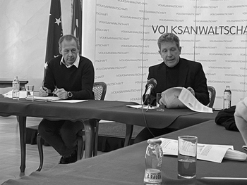 Gerald Herowitsch-Trinkl und Bernhard Achitz sitzend vor der Pressewand im Festsaal der Volksanwaltschaft.