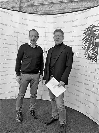 Gerald Herowitsch-Trinkl und Bernhard Achitz stehend vor der Pressewand im Festsaal der Volksanwaltschaft.