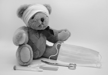 Teddybär mit Verband am Kopf, sitzend neben Schere, Maske, Pflaster und Testkit.