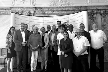 Group of 15 people in front of the press wall at the AOB in Vienna, consisting of 5 women and 10 men.