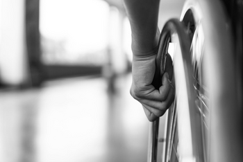 Eine Hand treibt das Rad eines Rollstuhls an.