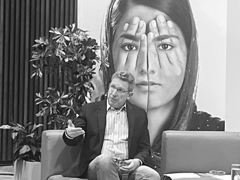 Bernhard Achitz sitzend auf grünen Sofas vor Schwarz-Weiß-Sujet von menschengroßen weiblichen Gesicht.